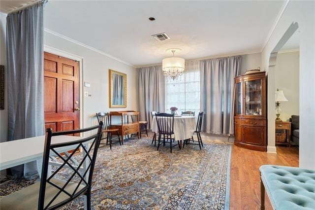 dining space with visible vents, a chandelier, wood finished floors, and ornamental molding