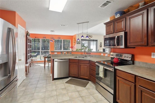 kitchen featuring decorative light fixtures, stainless steel appliances, visible vents, a sink, and a peninsula