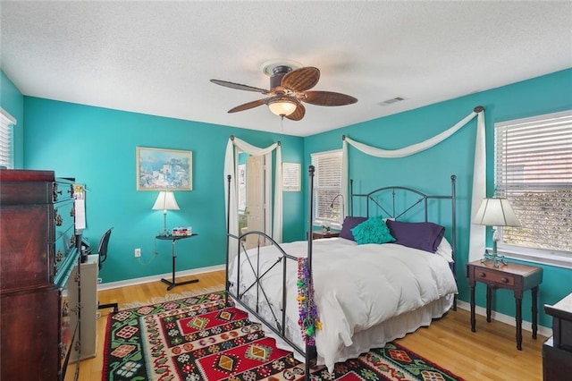 bedroom with ceiling fan, a textured ceiling, baseboards, and wood finished floors