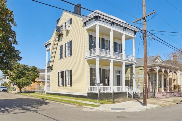 greek revival inspired property featuring a balcony, covered porch, and a chimney