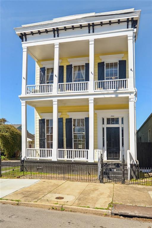 view of front facade featuring a porch, a balcony, and fence