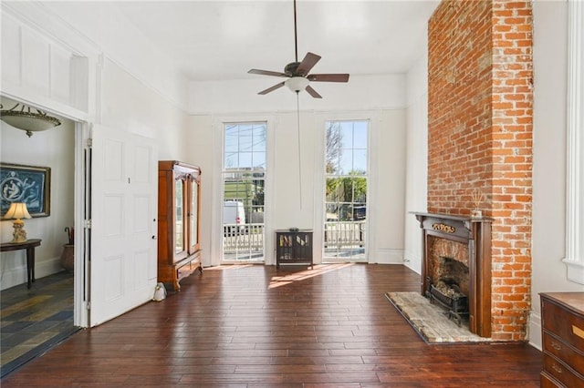 unfurnished living room with a towering ceiling, a fireplace, wood-type flooring, and ceiling fan