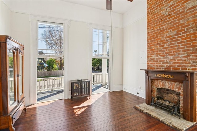 unfurnished living room featuring a brick fireplace, baseboards, a ceiling fan, and hardwood / wood-style flooring