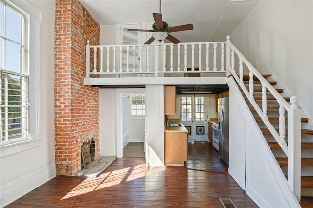 unfurnished living room featuring stairway, a brick fireplace, a ceiling fan, and dark wood-style flooring