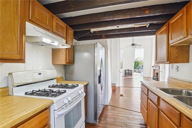 kitchen with white gas stove, beamed ceiling, light countertops, and under cabinet range hood