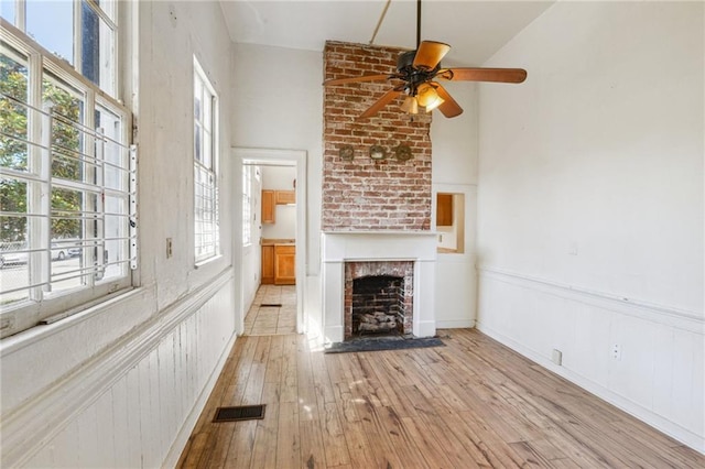 unfurnished living room featuring visible vents, a ceiling fan, light wood-style floors, wainscoting, and a fireplace