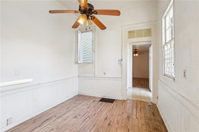 spare room featuring a wealth of natural light, light wood-type flooring, a wainscoted wall, and ceiling fan