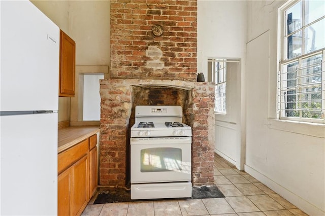 kitchen featuring white appliances, light tile patterned flooring, brown cabinetry, and light countertops