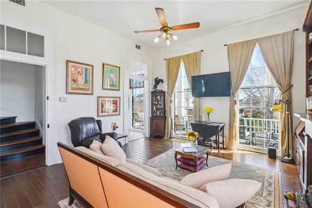 living room featuring ceiling fan, visible vents, dark wood-style floors, and stairway