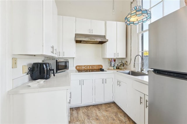 kitchen with a sink, light countertops, under cabinet range hood, and stainless steel appliances