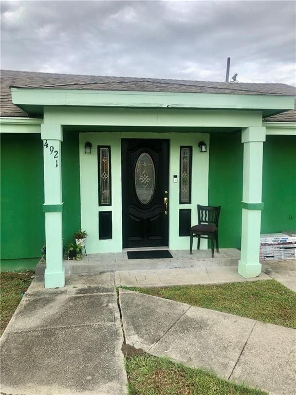 doorway to property featuring roof with shingles, a porch, and stucco siding