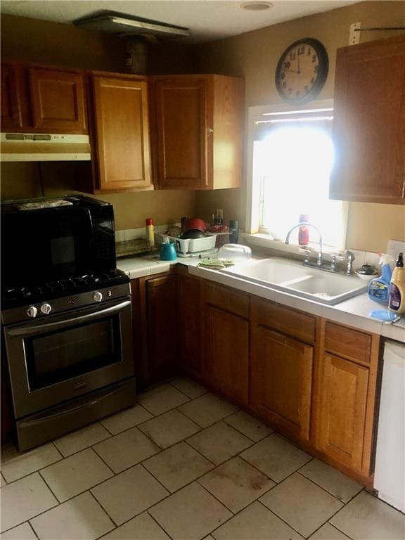 kitchen with under cabinet range hood, a sink, dishwasher, brown cabinetry, and stainless steel range with gas stovetop