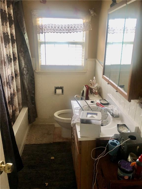 full bath featuring tile walls, shower / bathtub combination with curtain, vanity, and toilet