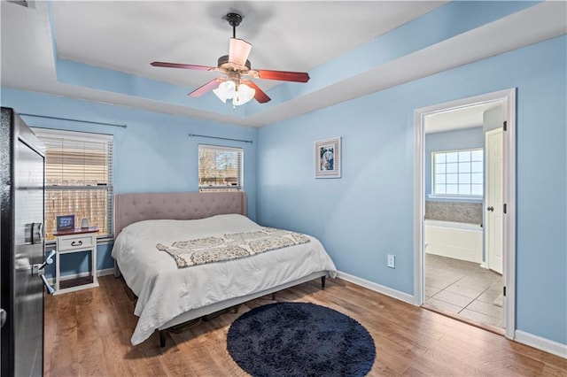 bedroom featuring wood finished floors, multiple windows, a raised ceiling, and baseboards