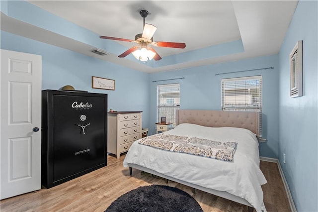 bedroom featuring wood finished floors, a ceiling fan, visible vents, baseboards, and a raised ceiling