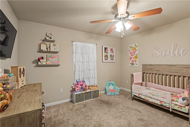 carpeted bedroom featuring a nursery area, a ceiling fan, and baseboards