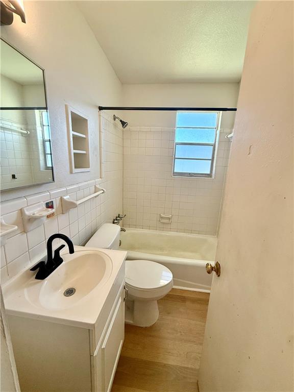 full bathroom with toilet, wood finished floors, vanity, tile walls, and shower / bathing tub combination