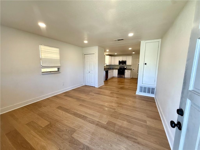 unfurnished living room with light wood finished floors, visible vents, baseboards, and a sink