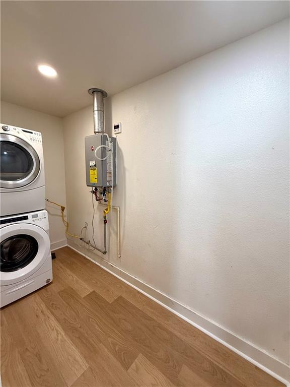 laundry room with water heater, stacked washing maching and dryer, wood finished floors, laundry area, and baseboards