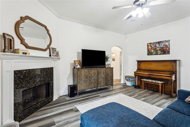 living room with arched walkways, a premium fireplace, wood finished floors, a ceiling fan, and ornamental molding