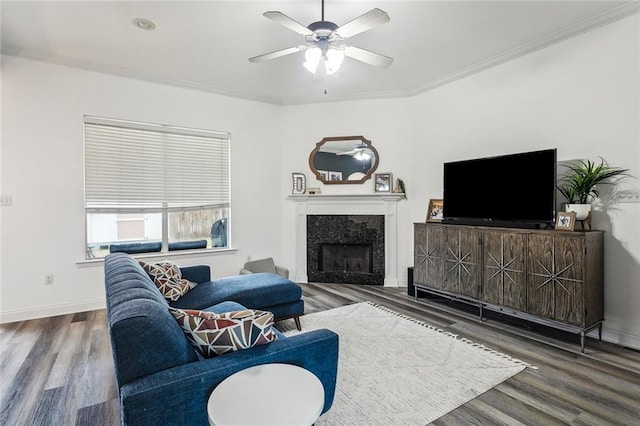 living room featuring ornamental molding, a high end fireplace, ceiling fan, wood finished floors, and baseboards