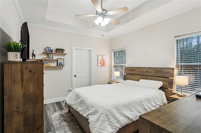 bedroom with baseboards, a raised ceiling, a ceiling fan, ornamental molding, and dark wood-type flooring