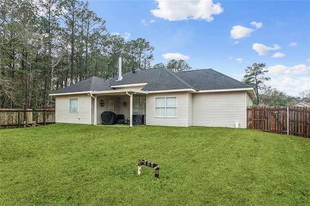 back of house with a shingled roof, a fenced backyard, and a lawn