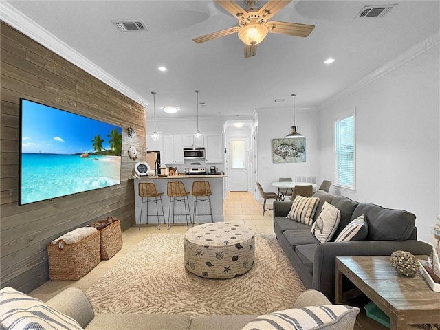 living room with ornamental molding, a ceiling fan, visible vents, and wooden walls