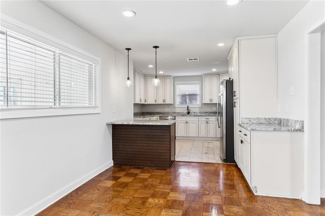 kitchen with light stone counters, recessed lighting, visible vents, freestanding refrigerator, and a peninsula