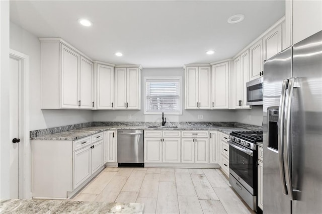 kitchen featuring light stone counters, recessed lighting, a sink, white cabinetry, and appliances with stainless steel finishes