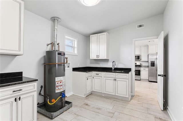 kitchen featuring gas water heater, a sink, visible vents, appliances with stainless steel finishes, and light wood finished floors