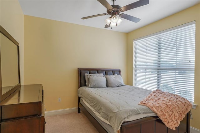 bedroom featuring light carpet, ceiling fan, multiple windows, and baseboards