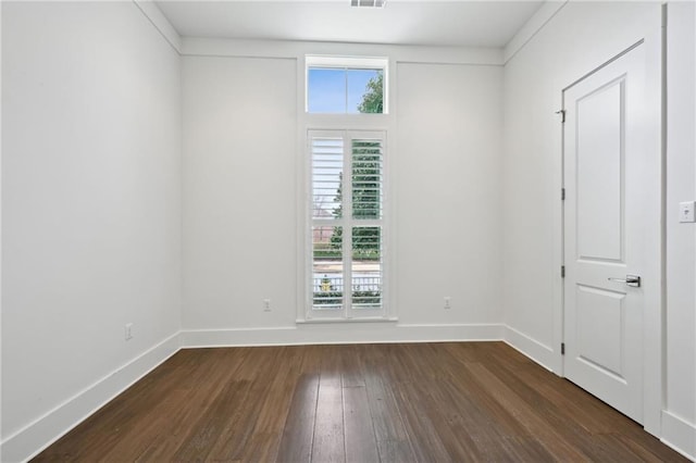 empty room featuring a healthy amount of sunlight, visible vents, baseboards, and dark wood finished floors