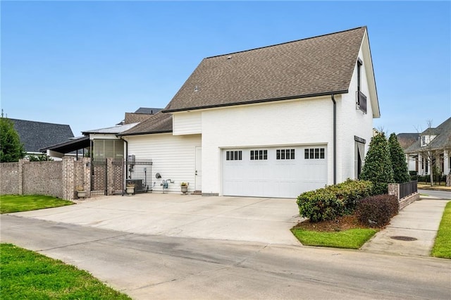 view of side of property featuring concrete driveway, roof with shingles, fence, and an attached garage