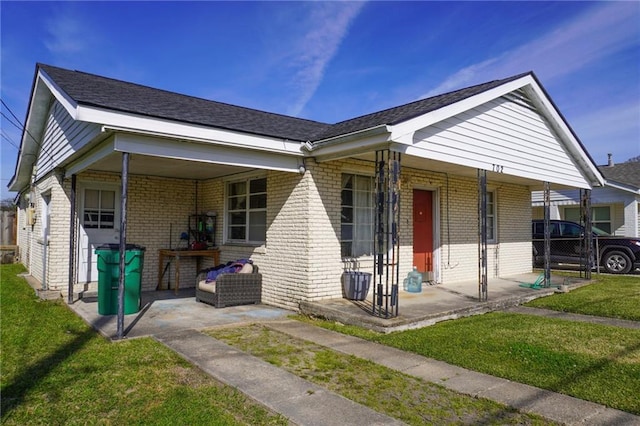 view of front of home featuring a porch, brick siding, fence, roof with shingles, and a front lawn