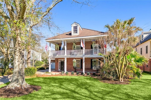 view of front facade with a front yard, covered porch, brick siding, and a balcony