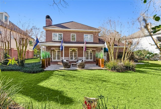 back of house featuring a yard, brick siding, french doors, and a chimney