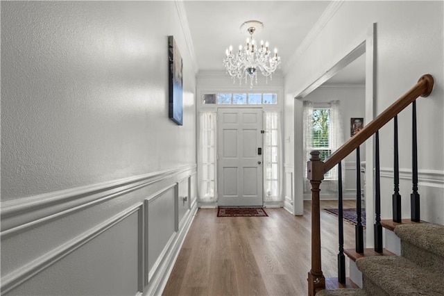 entryway featuring a wainscoted wall, a decorative wall, ornamental molding, wood finished floors, and stairs