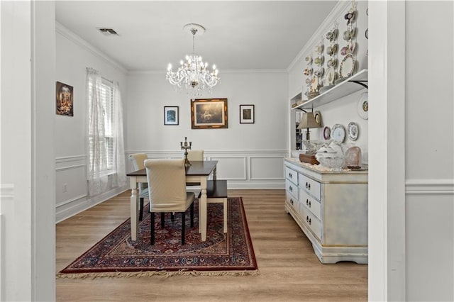 dining space featuring crown molding, light wood-type flooring, a notable chandelier, and a decorative wall