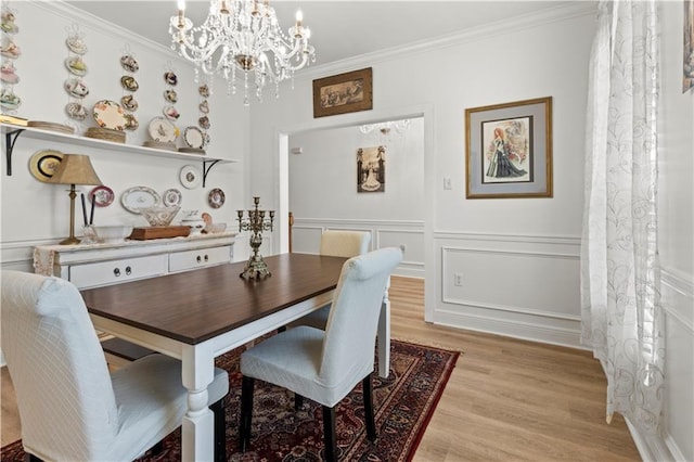 dining space with ornamental molding, light wood-type flooring, a chandelier, and a decorative wall