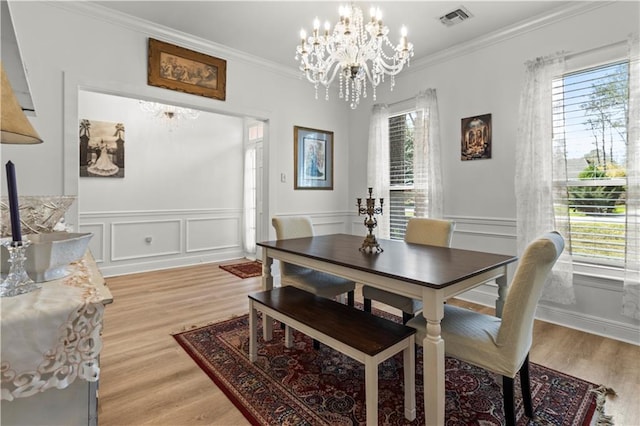 dining area with a wainscoted wall, a notable chandelier, visible vents, ornamental molding, and light wood-type flooring