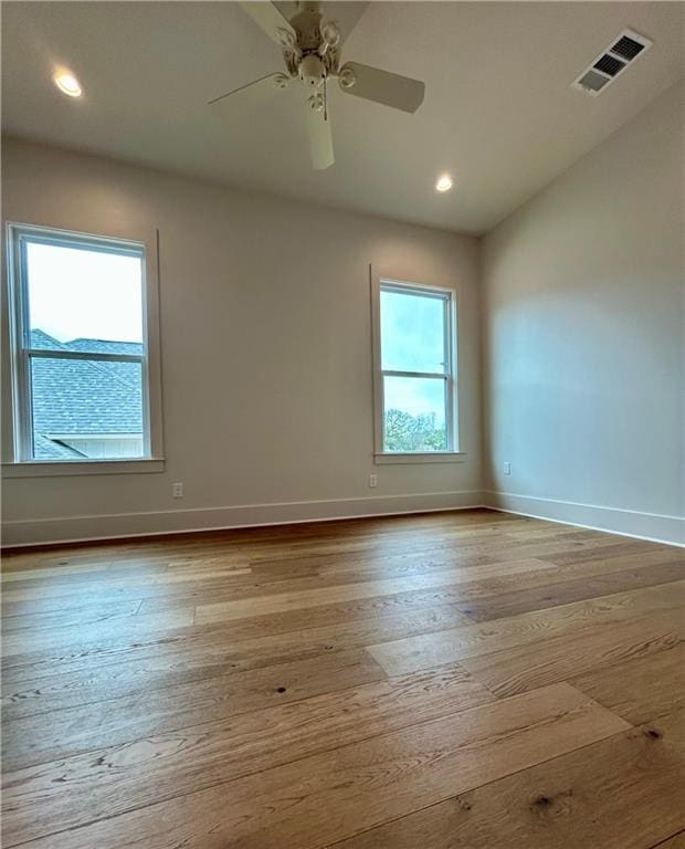 spare room with a ceiling fan, wood-type flooring, visible vents, and baseboards