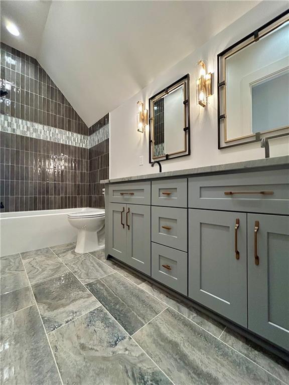 bathroom with double vanity, toilet, a sink, vaulted ceiling, and  shower combination