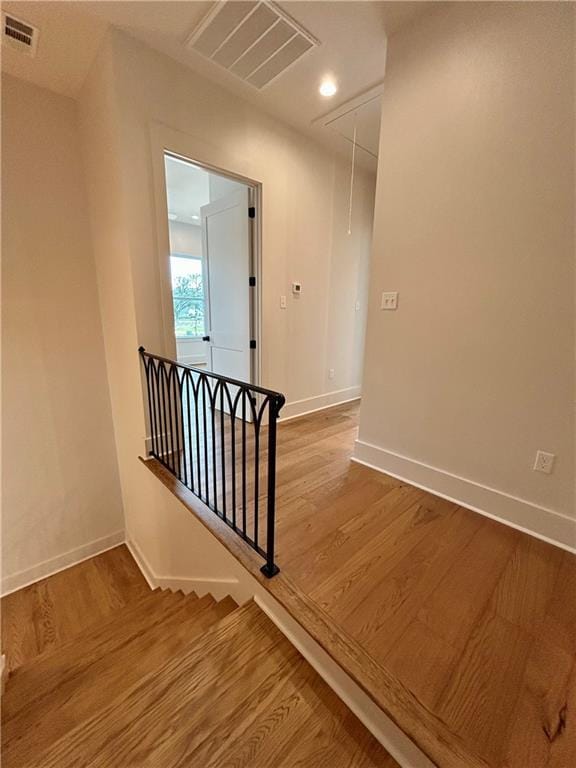 hallway with attic access, visible vents, wood finished floors, and an upstairs landing