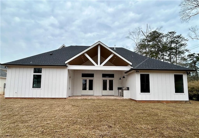 rear view of property featuring french doors, roof with shingles, a patio, a lawn, and board and batten siding