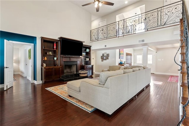 living room featuring a fireplace with raised hearth, baseboards, visible vents, and dark wood finished floors