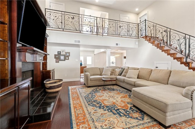 living area featuring baseboards, a fireplace with raised hearth, stairway, dark wood-type flooring, and a high ceiling