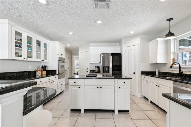 kitchen with stainless steel appliances, dark countertops, white cabinets, and visible vents