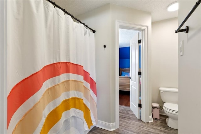 full bath with a shower with curtain, a textured ceiling, toilet, and wood finished floors