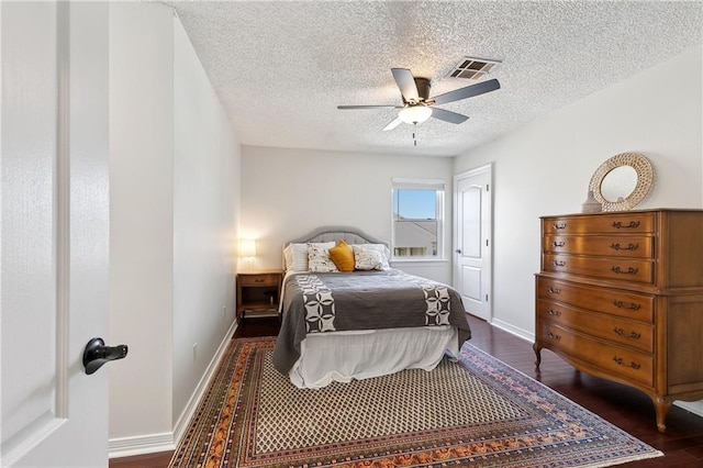 bedroom featuring dark wood-style flooring, visible vents, a ceiling fan, a textured ceiling, and baseboards